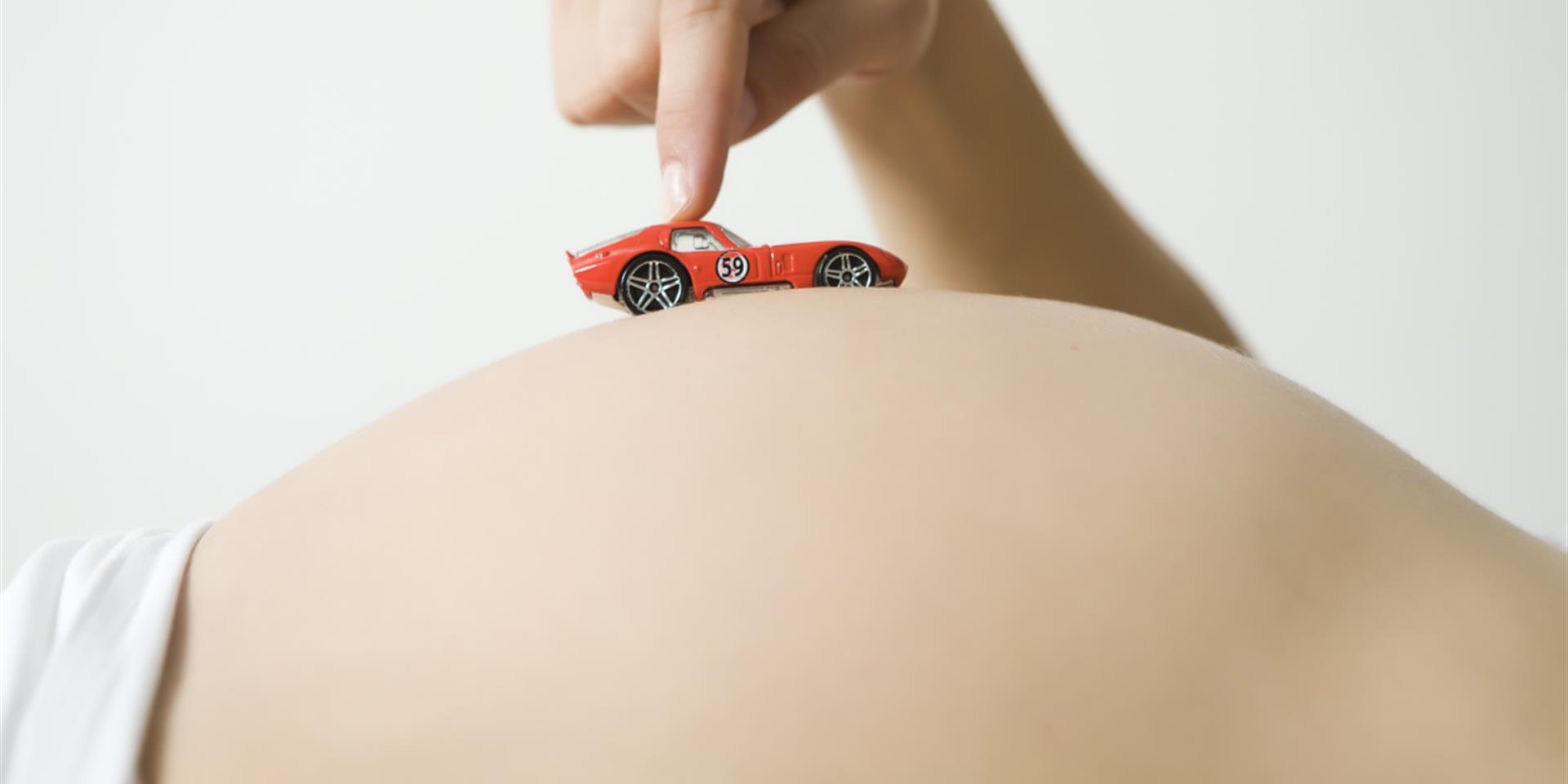 אישה בהיריון מסיעה מכונית צעצוע על הבטן שלה