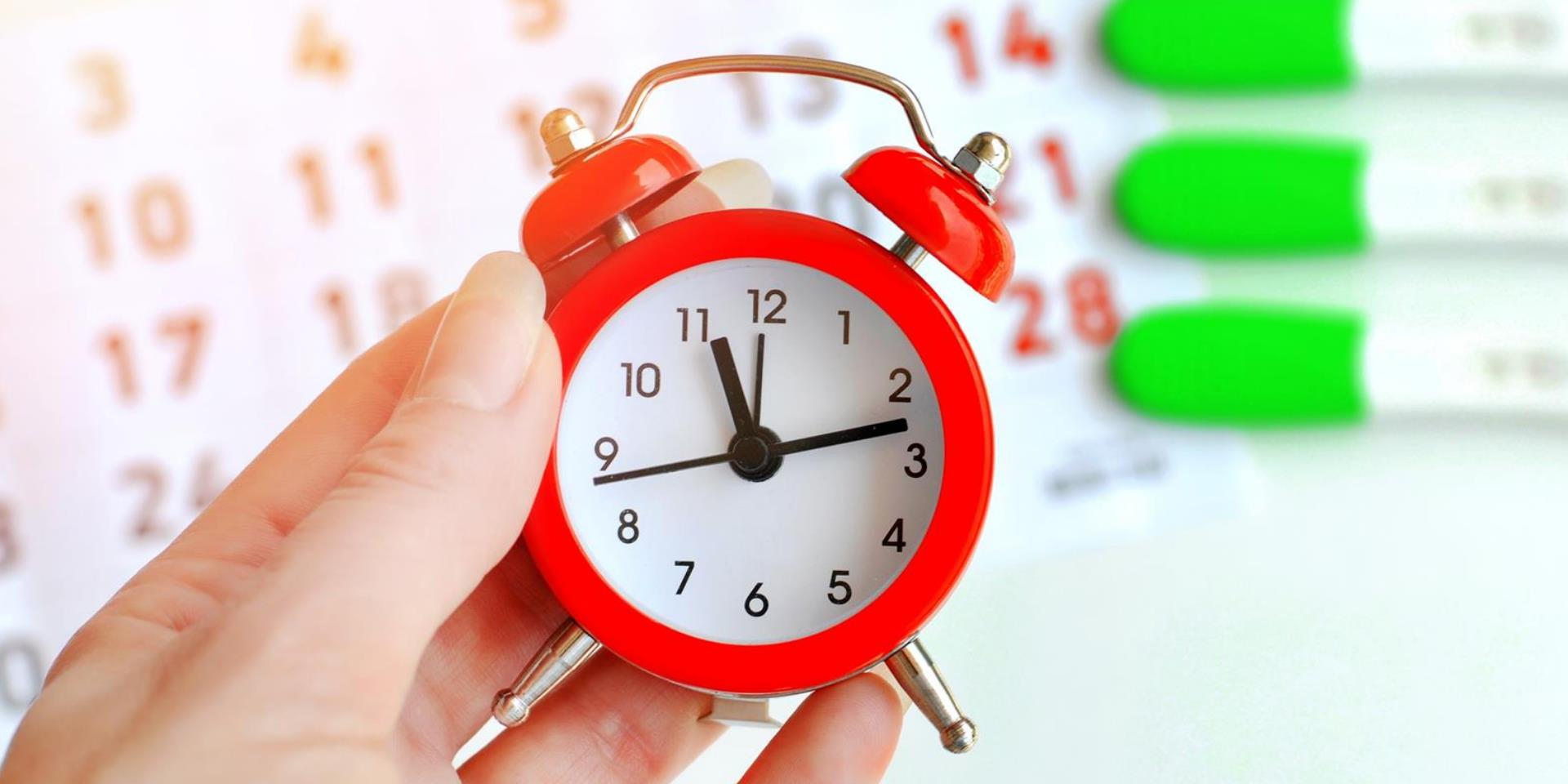 יד מחזיקה שעון על רקע ערכות לבדיקת היריון ולוח שנה