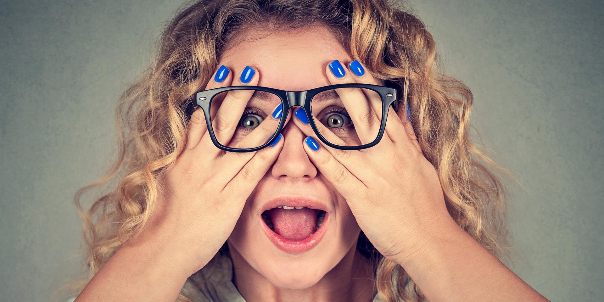 אישה שמרכיבה משקפיים מצמידה את ידיה אל העיניים ומביטה בין האצבעות