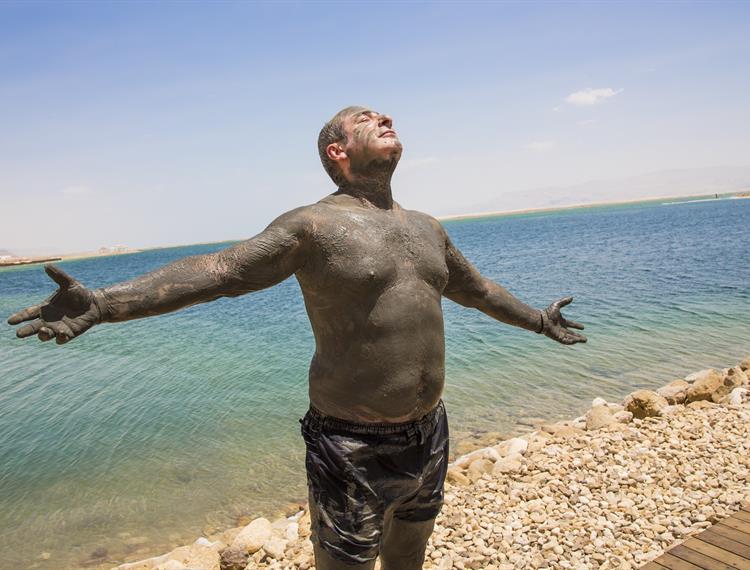בחור מניף ידיים לאוויר בזמן טיפול בבוץ בים המלח