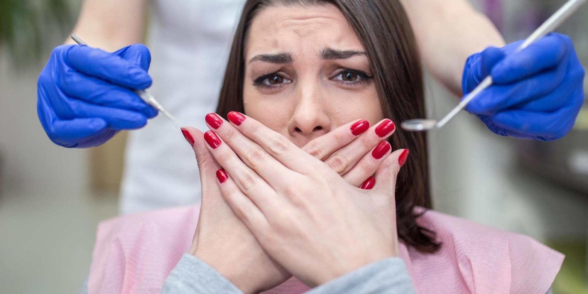 אישה מבוהלת עם חרדה דנטלית מסתירה את הפה כשרופאת שיניים מאחוריה