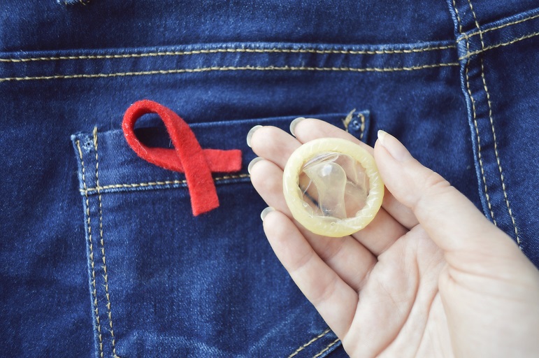 כף יד של בחורה מחזיקה קונדום על רקע ג'ינס בצבע כחול עם סרט אדום עליו